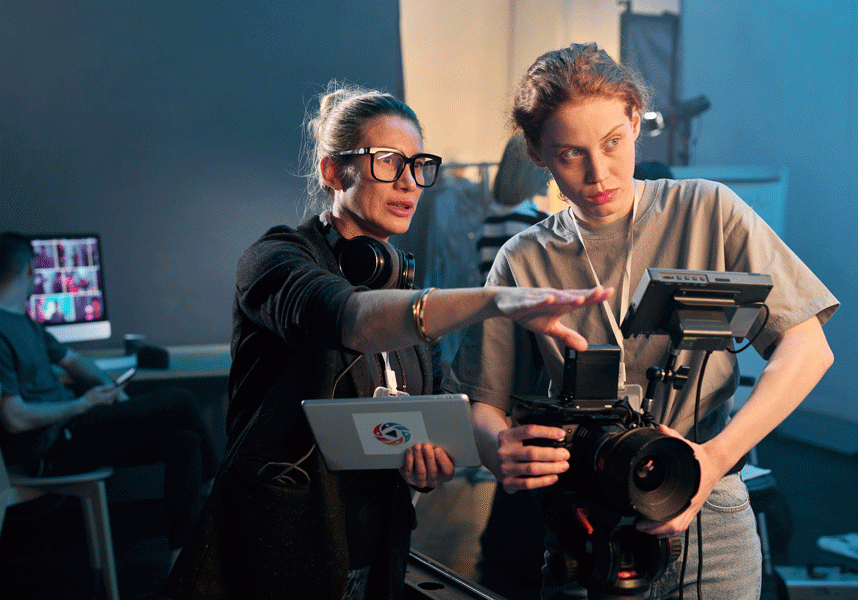 One woman holding a camera, one woman is holding an ipad directing her.